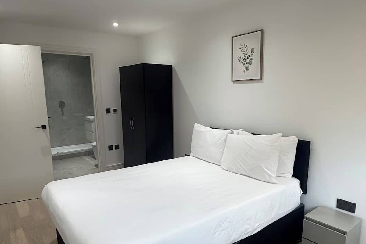 A modern bedroom with a large bed, a wardrobe, a bedside table, and a shower area.