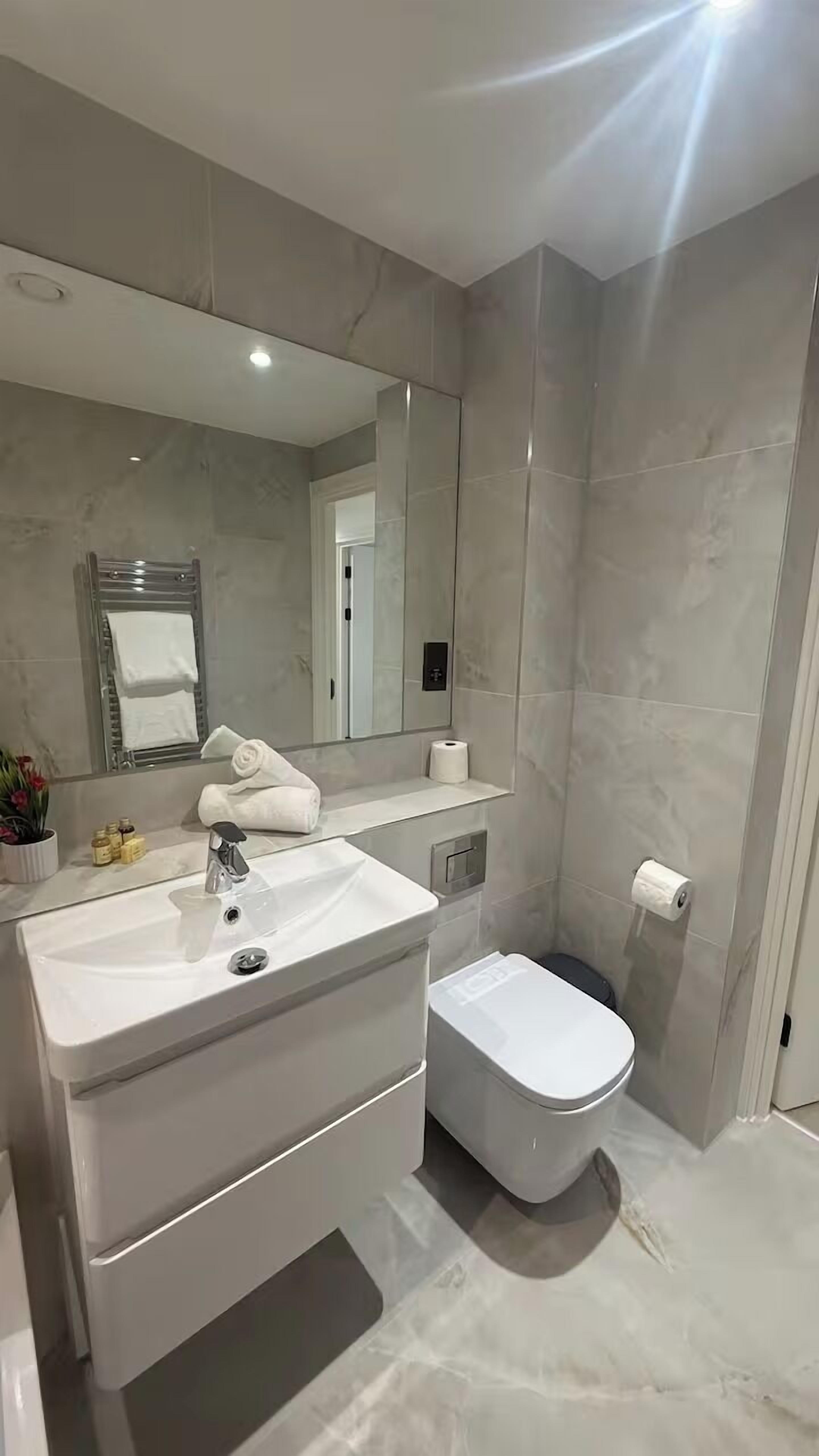 A modern bathroom with a large mirror, a white sink, a toilet, and a towel rack.