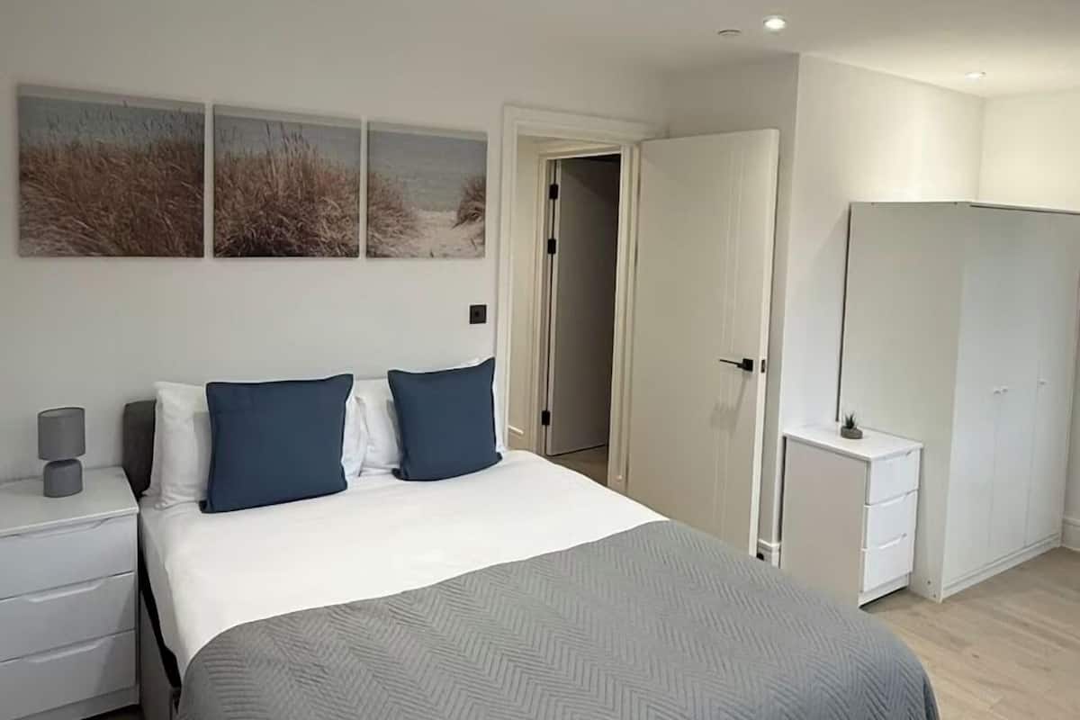 A modern bedroom with a large bed, a bedside table, a wardrobe, and a door leading to another room.