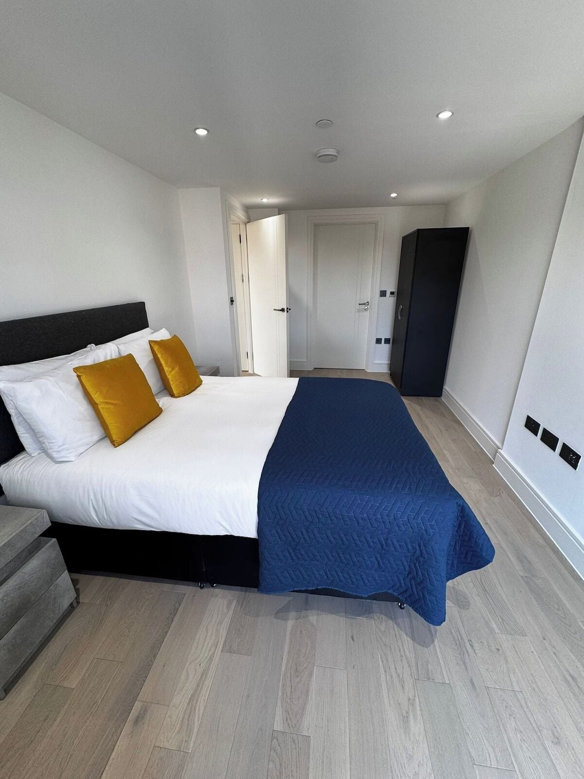A modern hotel room with a large bed, a wardrobe, and a door leading to another room.