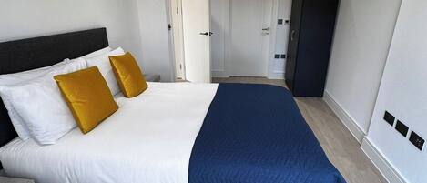 A modern hotel room with a large bed, a wardrobe, and a door leading to another room.