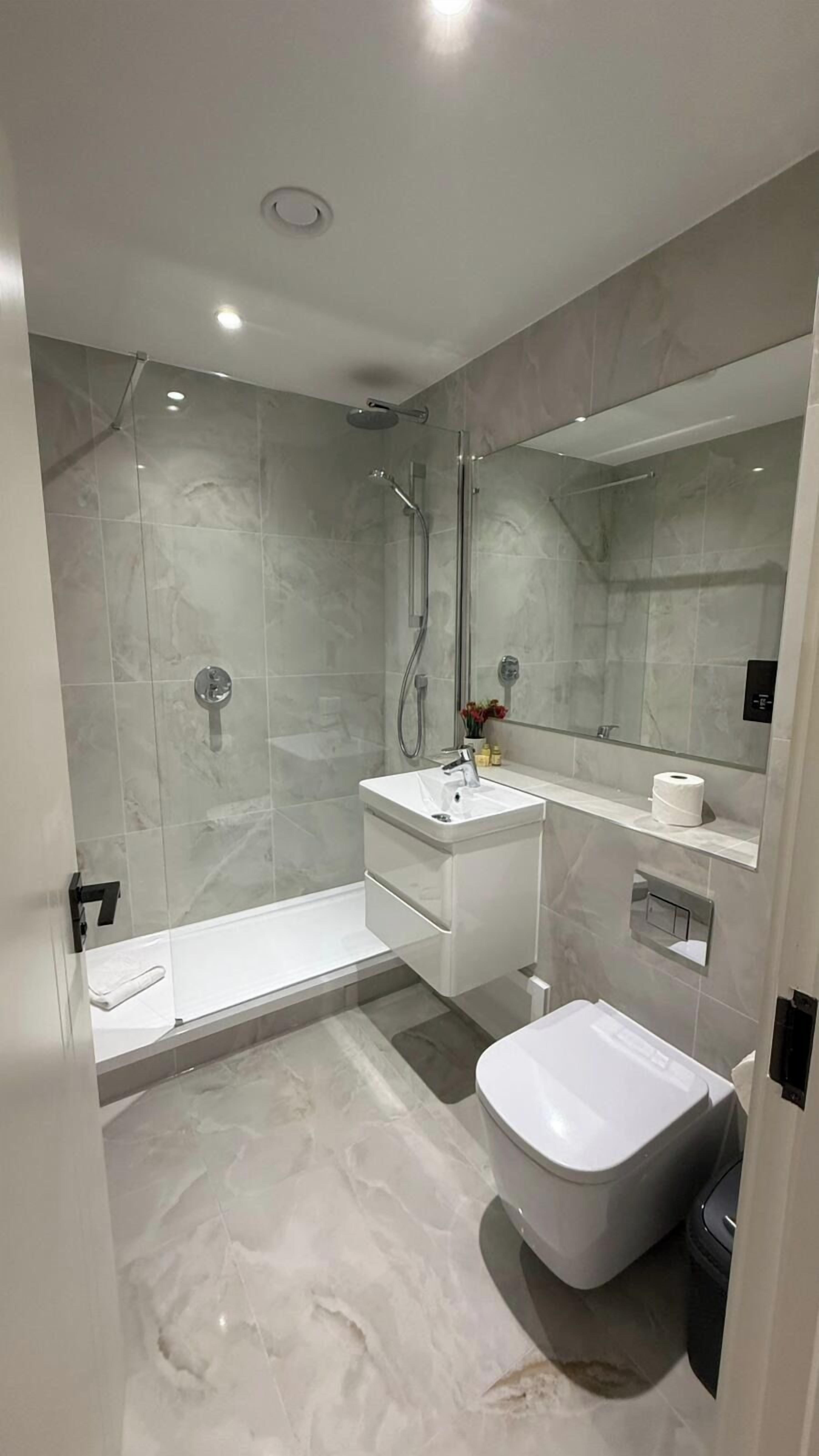 A modern bathroom with a glass-enclosed shower, a white sink, a bidet, and a large mirror.