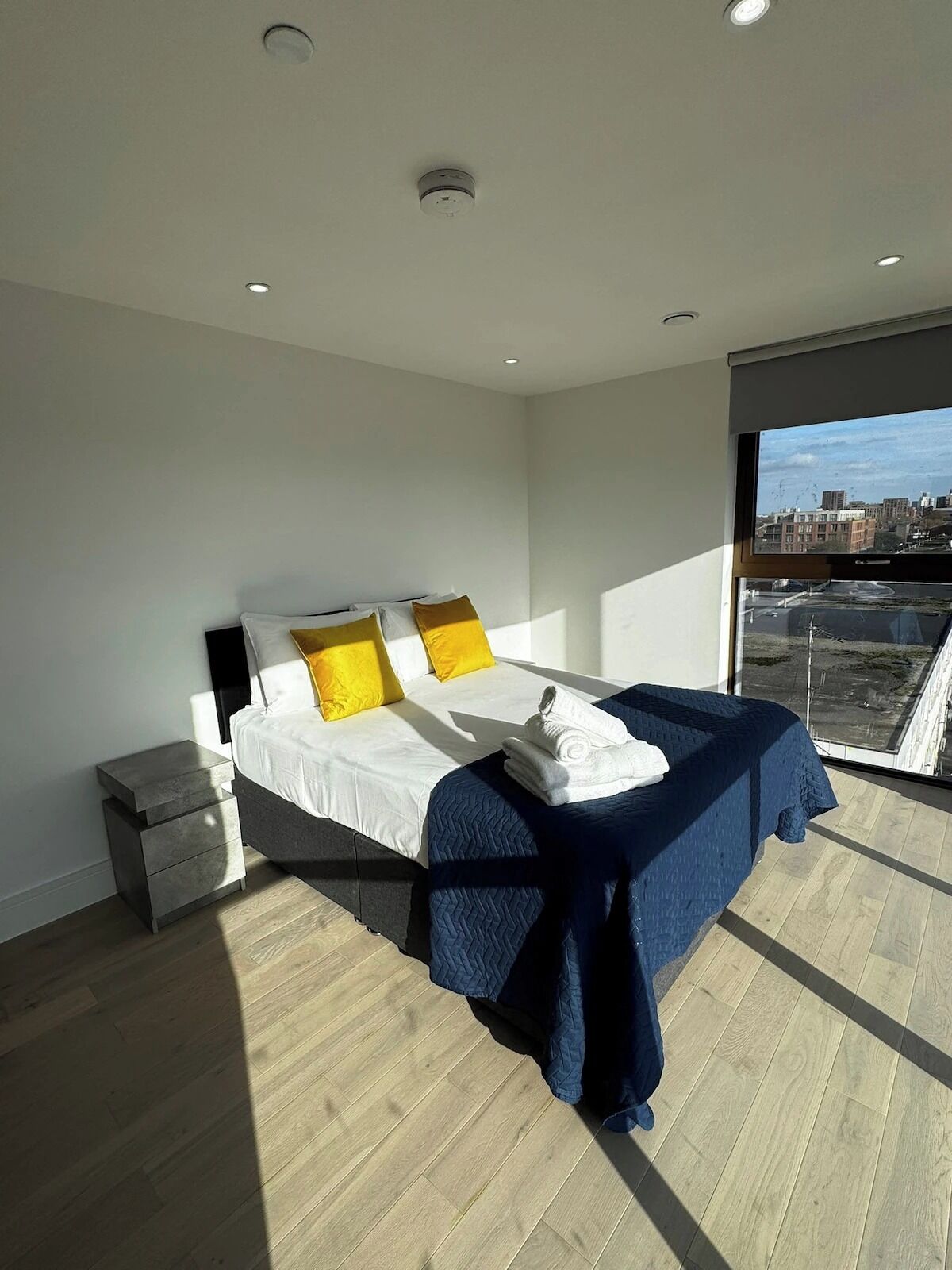 Une chambre à coucher moderne, avec un lit, une table de chevet et une vue sur la ville grâce à une grande fenêtre.