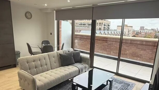Ein modernes Wohnzimmer mit einer Couch, einem Couchtisch und Blick auf die Stadt durch große Fenster.