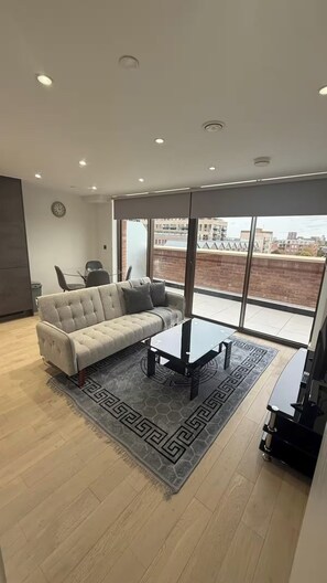 A modern living room with a sofa, coffee table, and a view of the city through large windows. - USTAY Barking (London)