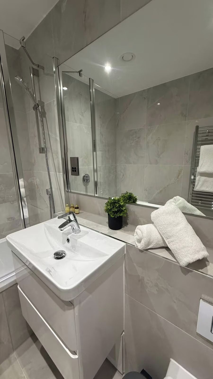 A modern bathroom with a large mirror, a shower, and a sink.