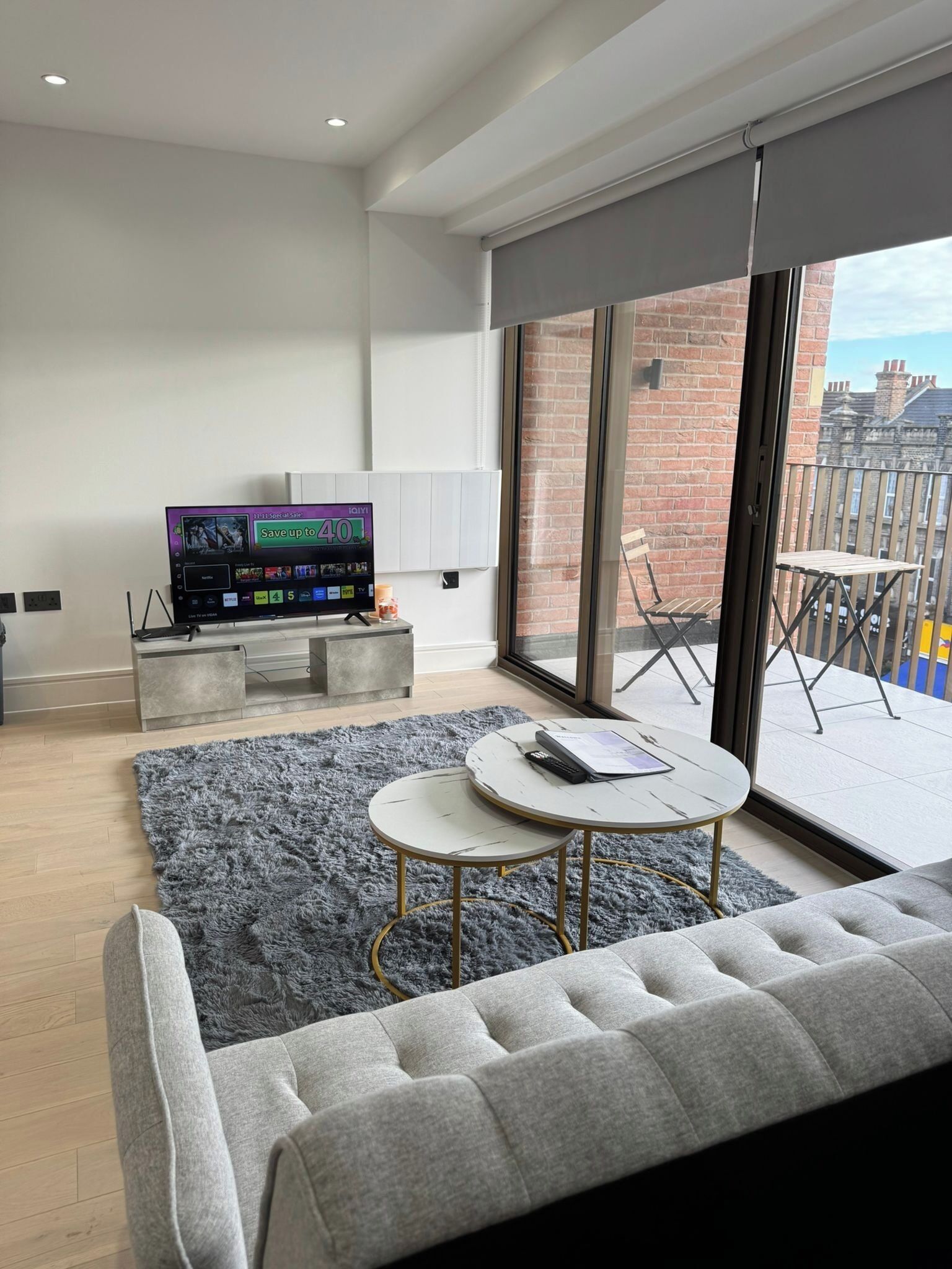 Ein modernes Wohnzimmer mit einem grauen Sofa, einem runden Couchtisch, einem Flachbildfernseher und einem grauen, flauschigen Teppich.
