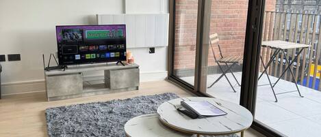Ein modernes Wohnzimmer mit einem grauen Sofa, einem runden Couchtisch, einem Flachbildfernseher und einem grauen, flauschigen Teppich.