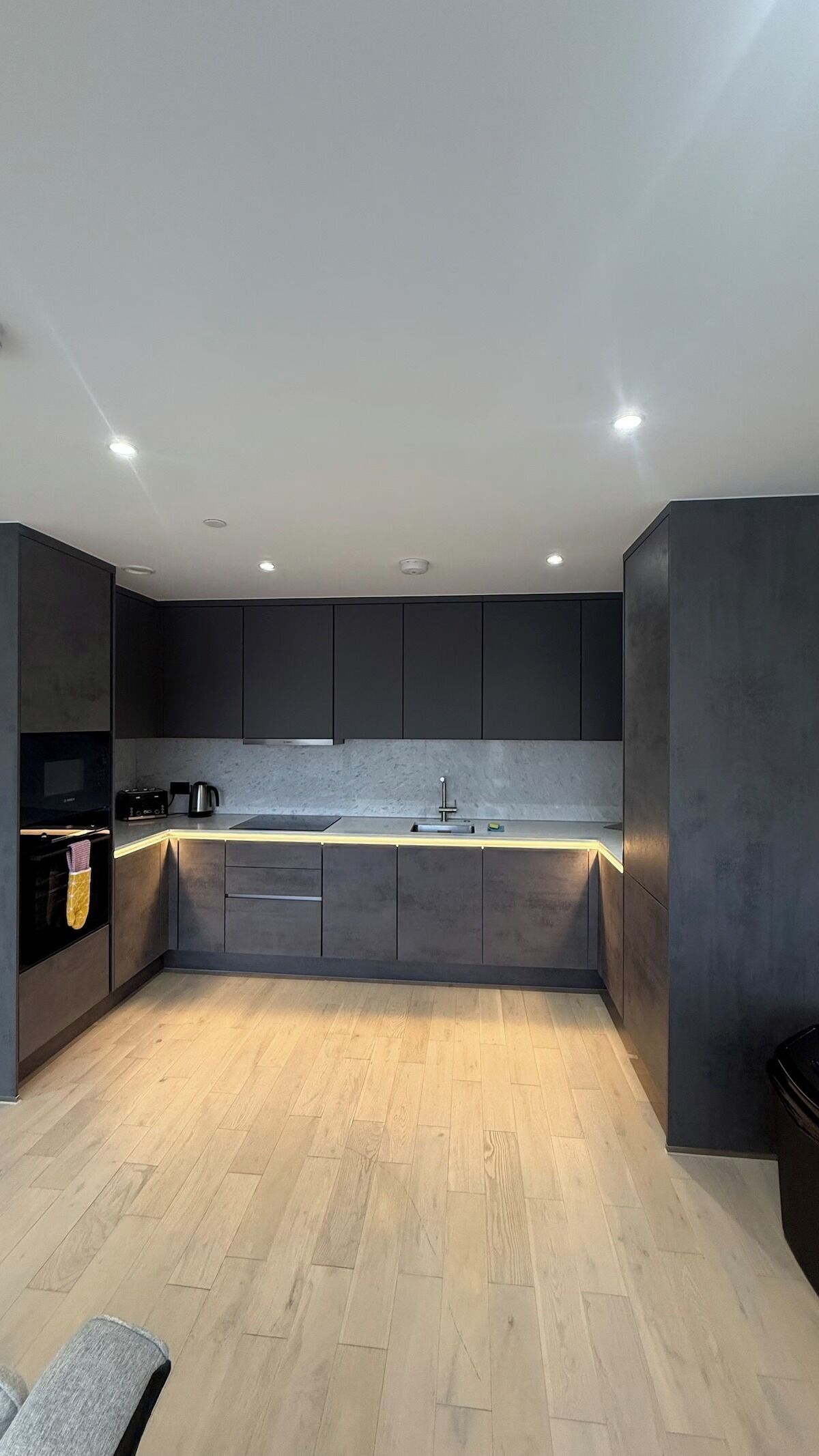 A modern kitchen with dark cabinetry, a central island, and a light wood floor.