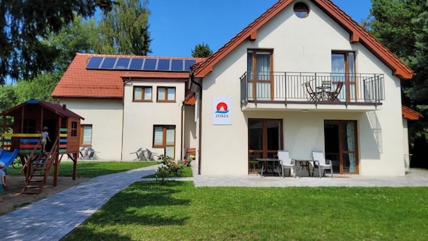 A two-story building with a red roof, a balcony, and a sign with a red circle and white background. - ZORZA (Sztutowo)