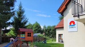 A children's play area with a slide and a small wooden structure, adjacent to a building with a sign reading "ZORZA". - ZORZA (Sztutowo)