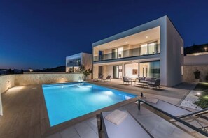 Ein modernes, zweistöckiges Haus mit Swimmingpool und Sitzgelegenheit im Freien.