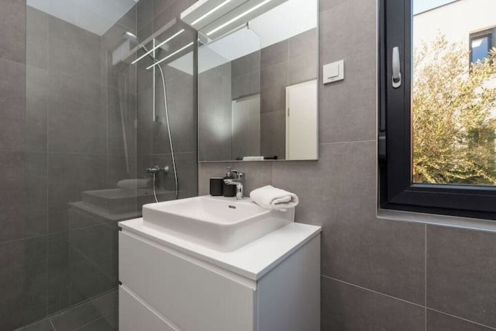 Une salle de bain moderne avec un grand miroir, un lavabo blanc et une douche à parois de verre.