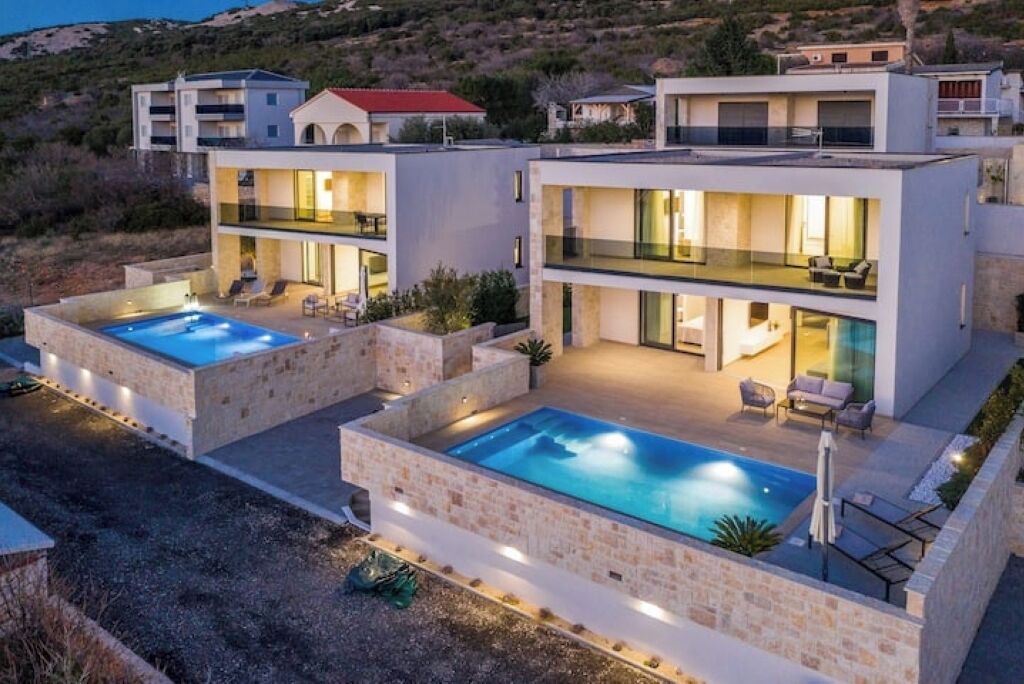 A modern two-story house with a swimming pool, outdoor seating, and a view of the surrounding landscape.