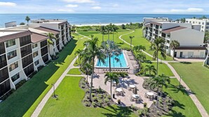 Een resort met een centraal zwembad, palmbomen en uitzicht op de oceaan.