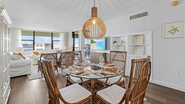 Een eetgedeelte met een ronde glazen tafel, rieten stoelen en een hanglamp.