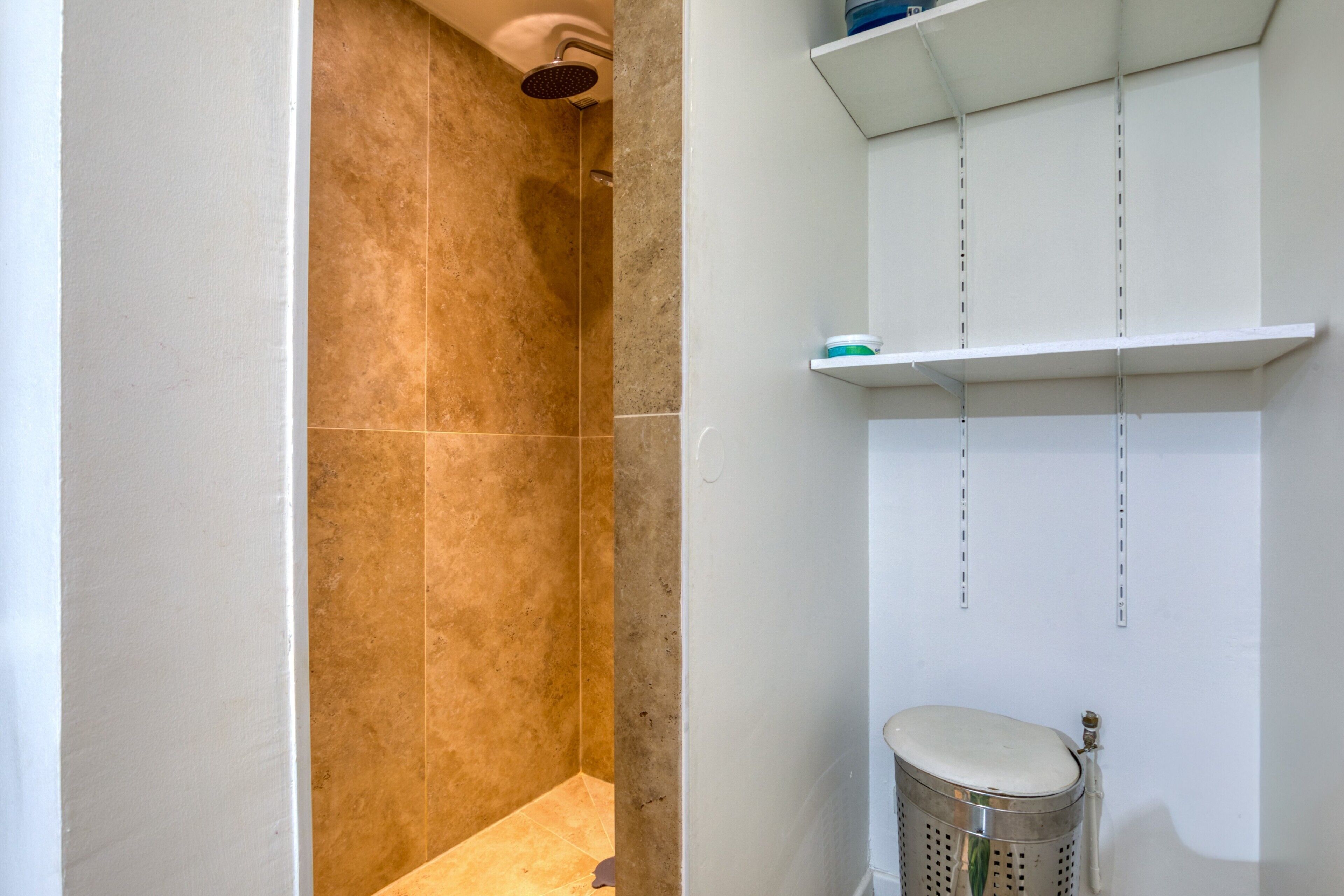 Une salle de bain équipée d’une douche, de toilettes et d’une étagère où sont rangés les articles de toilette.