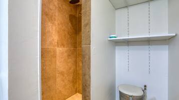 Une salle de bain équipée d’une douche, de toilettes et d’une étagère où sont rangés les articles de toilette.