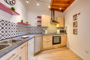 Een compacte keuken met een magnetron, oven en spoelbak. Er zijn houten keukenkastjes en een decoratieve spatelwand.