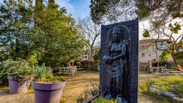 A garden with a statue, potted plants, and outdoor seating. - Gîte Acacia - Domaine de l'Enclos (Mireval)