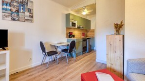 Un espacio habitable compacto con zona de comedor, kitchenette y televisor sobre un soporte.