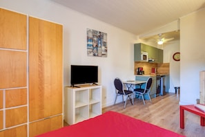 Ein Zimmer mit einem Bett, einem Fernseher, einem Schreibtisch mit Stühlen, einer Küchenzeile und einem roten Tisch.