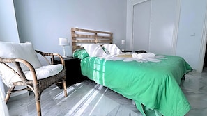 Ein Zimmer mit einem Bett, einem Sessel, einem Nachttisch und einer Tür.