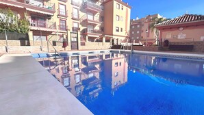 Una piscina con superficie de agua azul cristalina, rodeada de edificios de varios pisos con balcones y un techo de tejas.