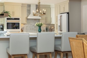 Cocina moderna con una isla central, muebles blancos, electrodomésticos de acero inoxidable y una lámpara colgante.