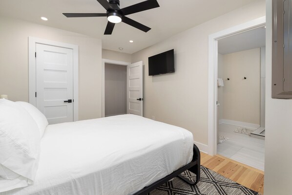 Un dormitorio con cama, ventilador de techo, televisión y puerta de baño.