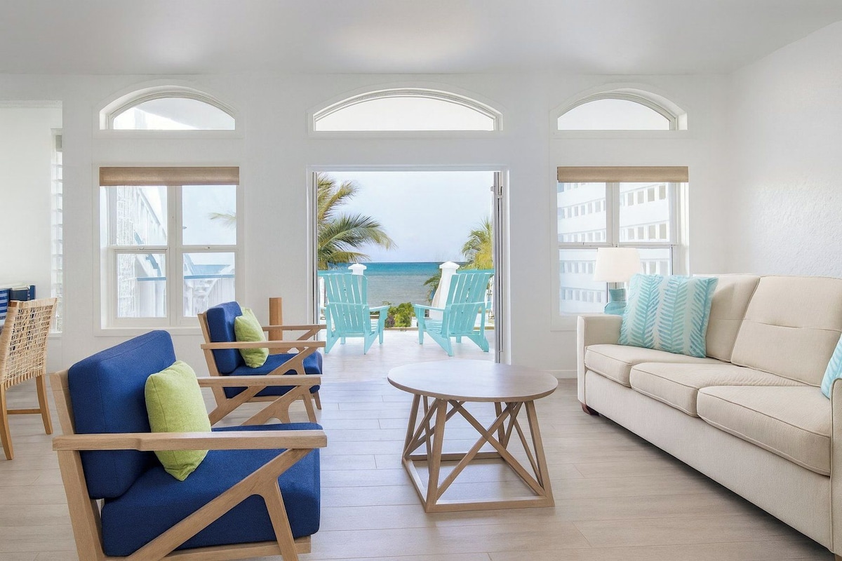 A room with a view of the ocean, featuring a sofa, chairs, and a small table.