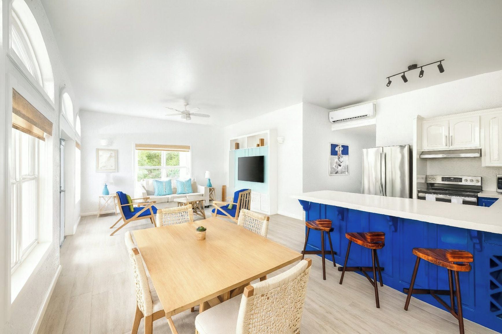 Une cuisine moderne avec des meubles blancs, un coin bar bleu et un espace repas avec une table en bois et des chaises en osier.