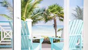 A deck with light blue Adirondack chairs overlooking a beach with palm trees and the ocean. - Reef Haven Belize (San Pedro)