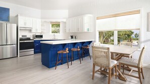A modern kitchen with white cabinets, a blue island, stainless steel appliances, and a dining area with wicker chairs. - Reef Haven Belize (San Pedro)