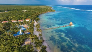 An aerial view of a coastal resort with multiple buildings, a pier extending into the ocean, and a beach area. - Reef Haven Belize (San Pedro)