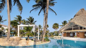 A pool area with palm trees, a thatched-roof structure, and lounge chairs. - Reef Haven Belize (San Pedro)