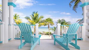 Two turquoise Adirondack chairs facing a beach with palm trees and a clear sky. - Reef Haven Belize (San Pedro)