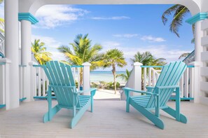 Two turquoise Adirondack chairs facing a beach with palm trees and a clear sky. - Reef Haven Belize (San Pedro)