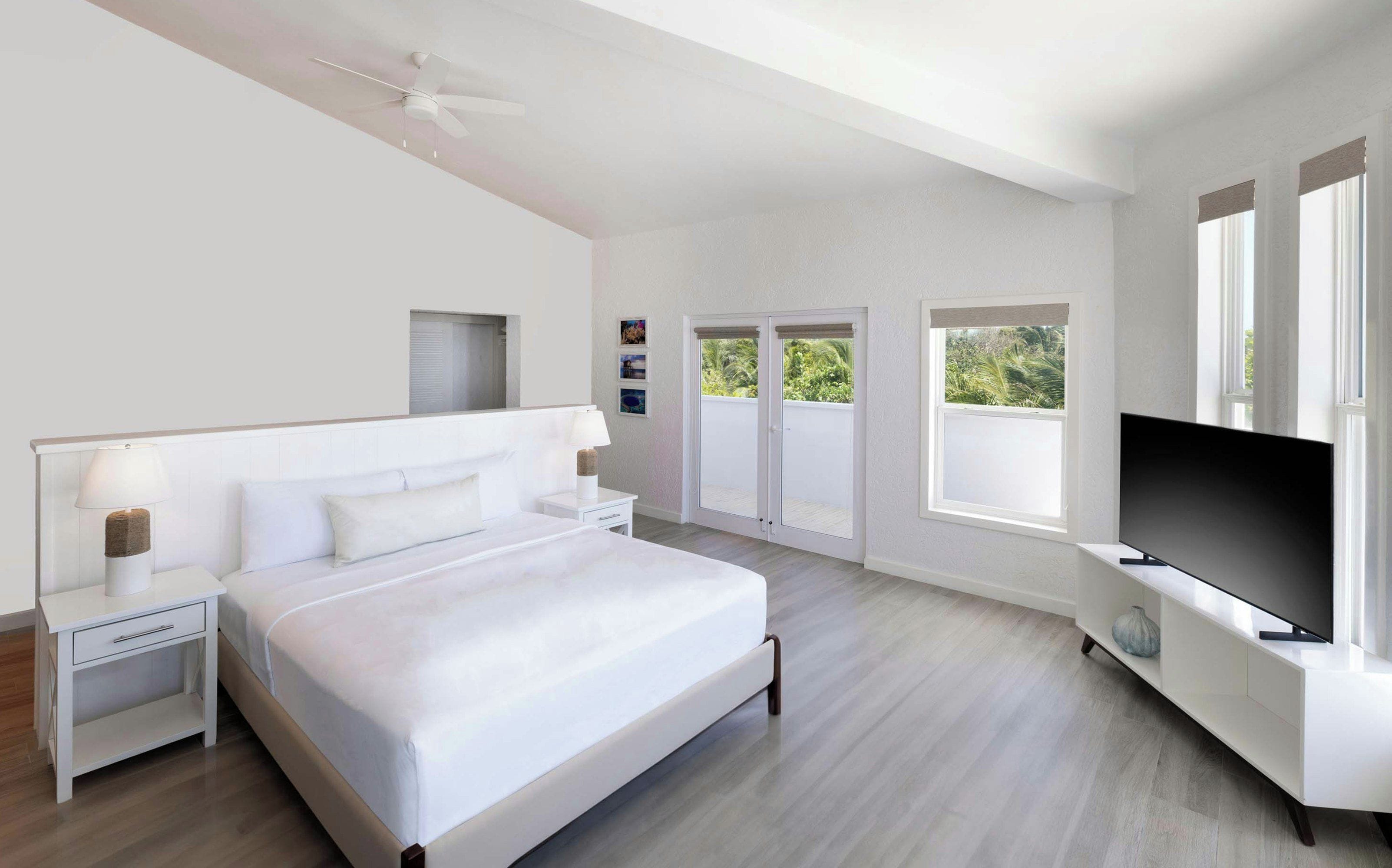 A modern bedroom with a bed, bedside tables, a ceiling fan, a TV, and a balcony with sliding doors.