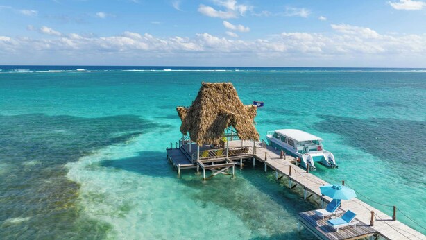 A thatched-roof structure on a pier with clear turquoise water, a boat docked at the end, and a clear sky. - Reef Haven Belize (San Pedro)