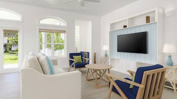 A spacious living room with a white sofa, blue armchairs, a coffee table, and a flat-screen TV mounted on the wall.