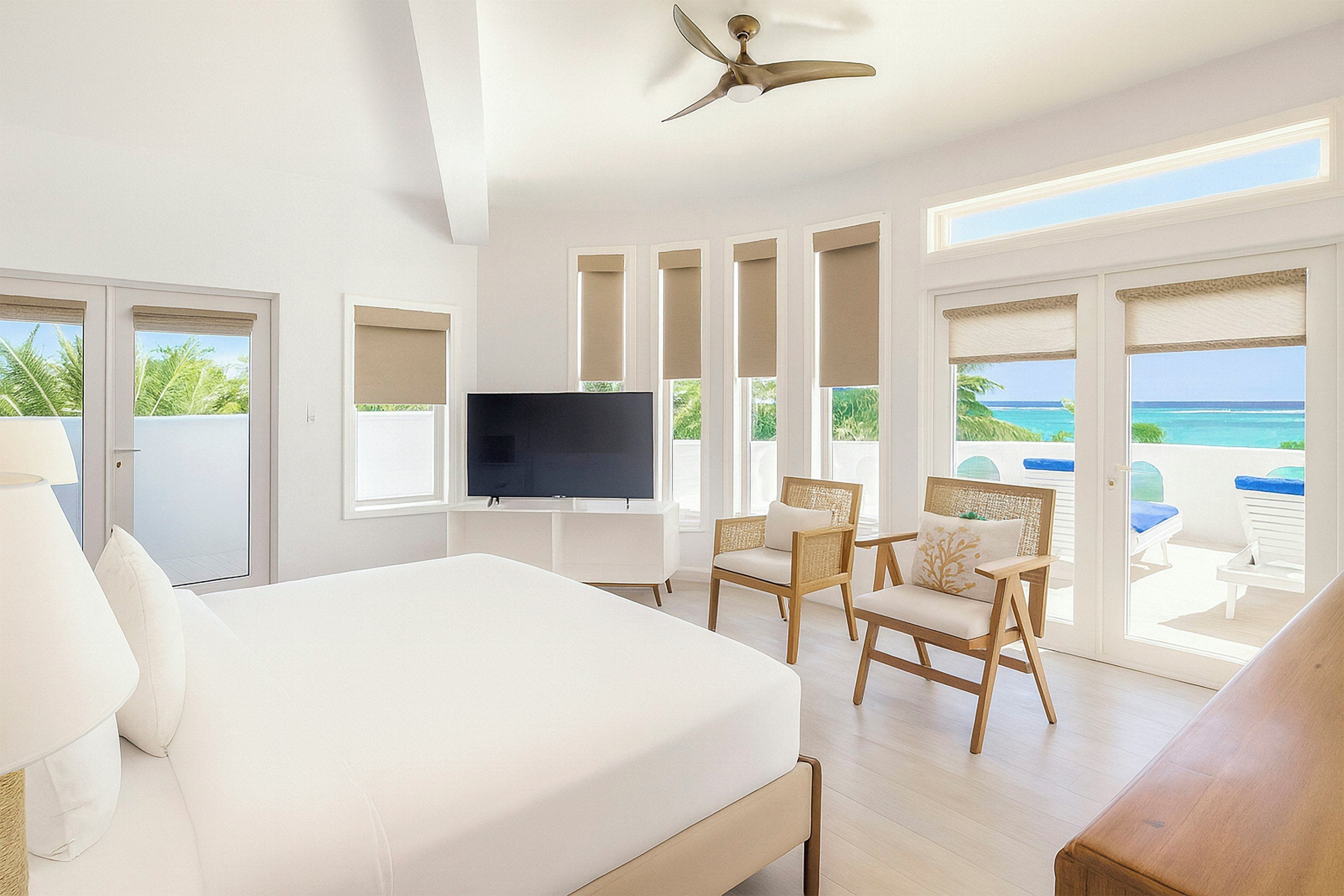 Ein Hotelzimmer mit Bett, Fernseher, Deckenventilator und Blick auf den Ozean.