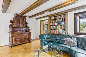 A room with a wooden cabinet, a leather sofa, a glass coffee table, and a bookshelf filled with books. - Apartment 'Fewo Wrede am Sauerland-Radring 1' with Mountain View, Private Terrace & Wi-Fi (Eslohe)