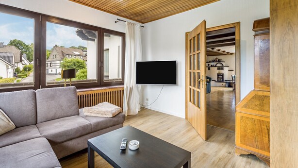 Uma sala de estar moderna com um sofá, uma mesa de centro, uma TV de tela plana na parede e um armário de madeira.