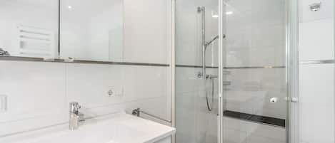 Un baño moderno con ducha envuelta en cristal, un lavamanos blanco y un espejo.