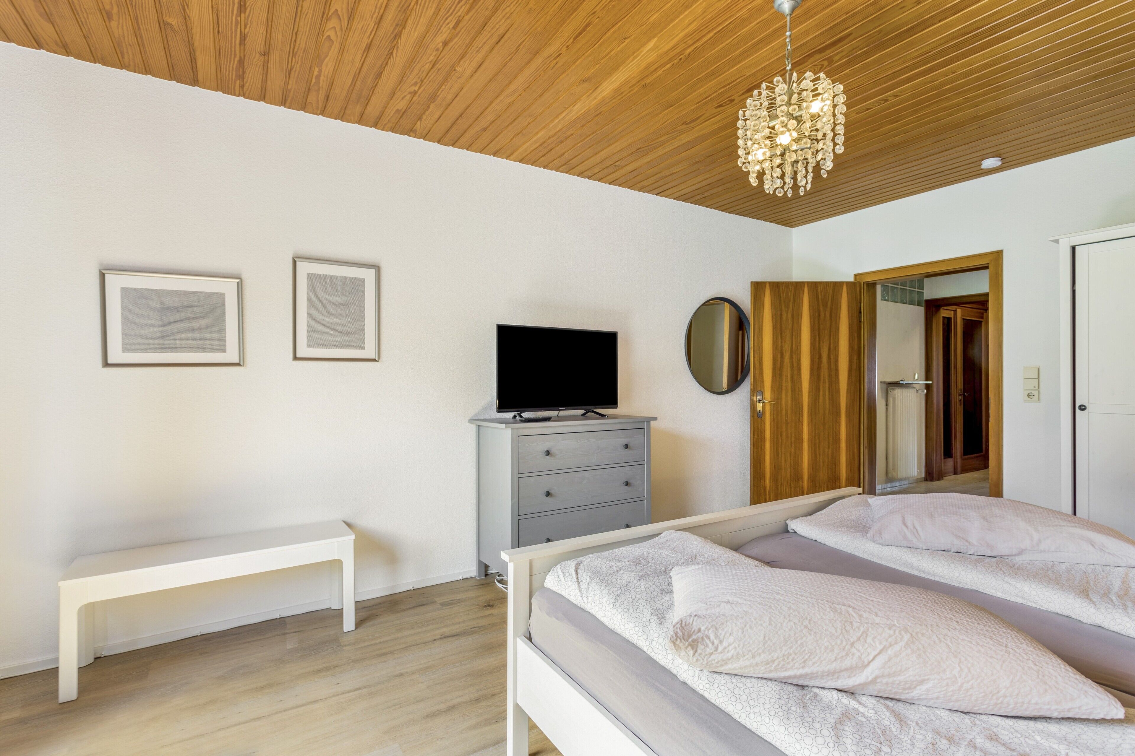 Ein Schlafzimmer mit einem Bett, einer Sitzbank, einem Schminktisch, einem Fernseher und einem Spiegel.