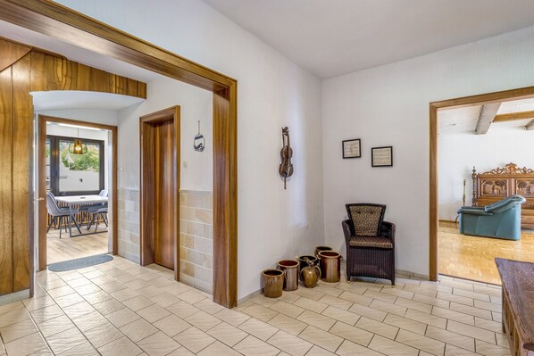 Un pasillo amplio con puerta de madera, una zona de estar con una silla y un comedor con mesa y sillas.
