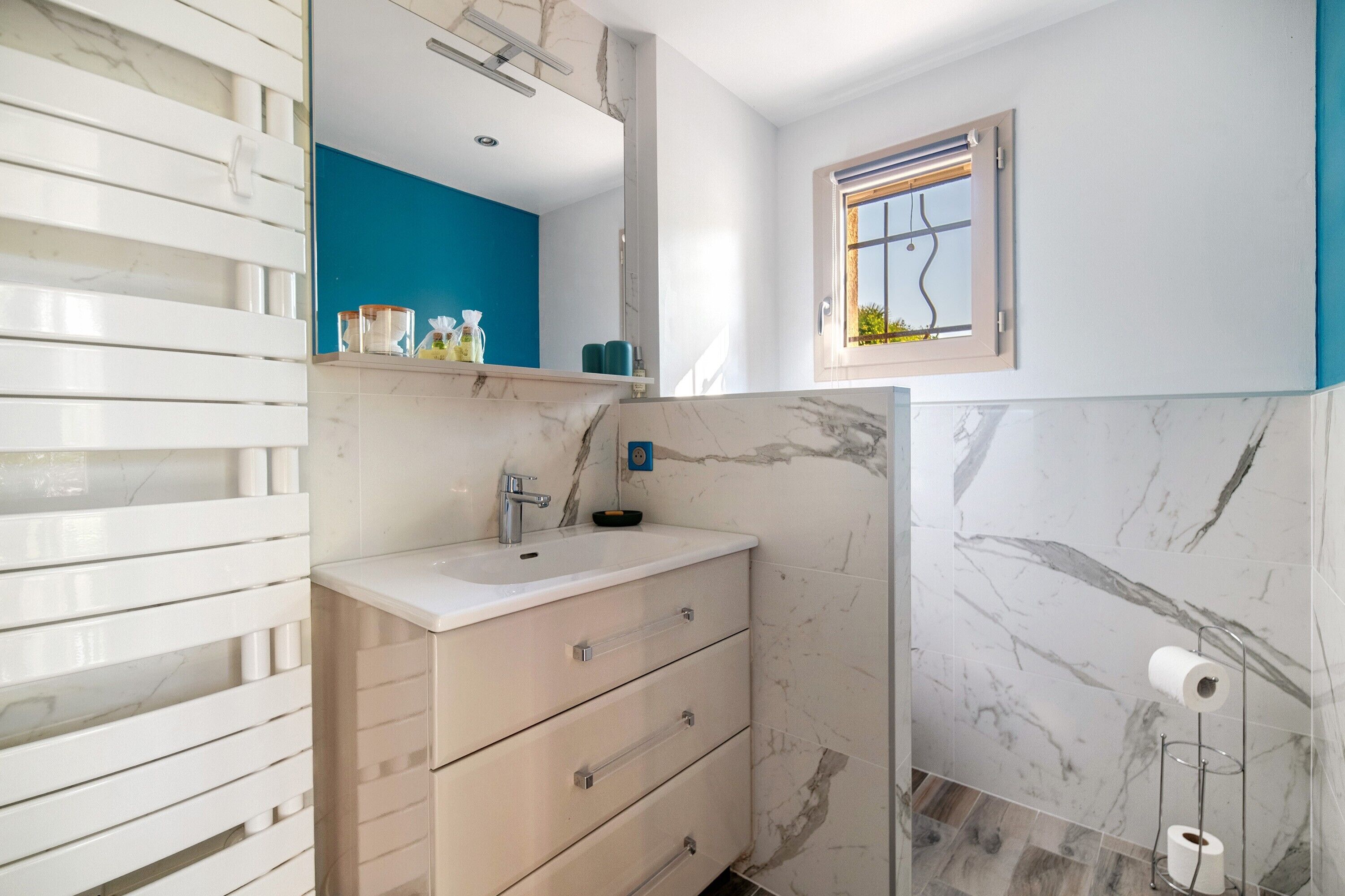 A bathroom with a white sink, marble walls, a blue accent wall, a mirror, and a window.