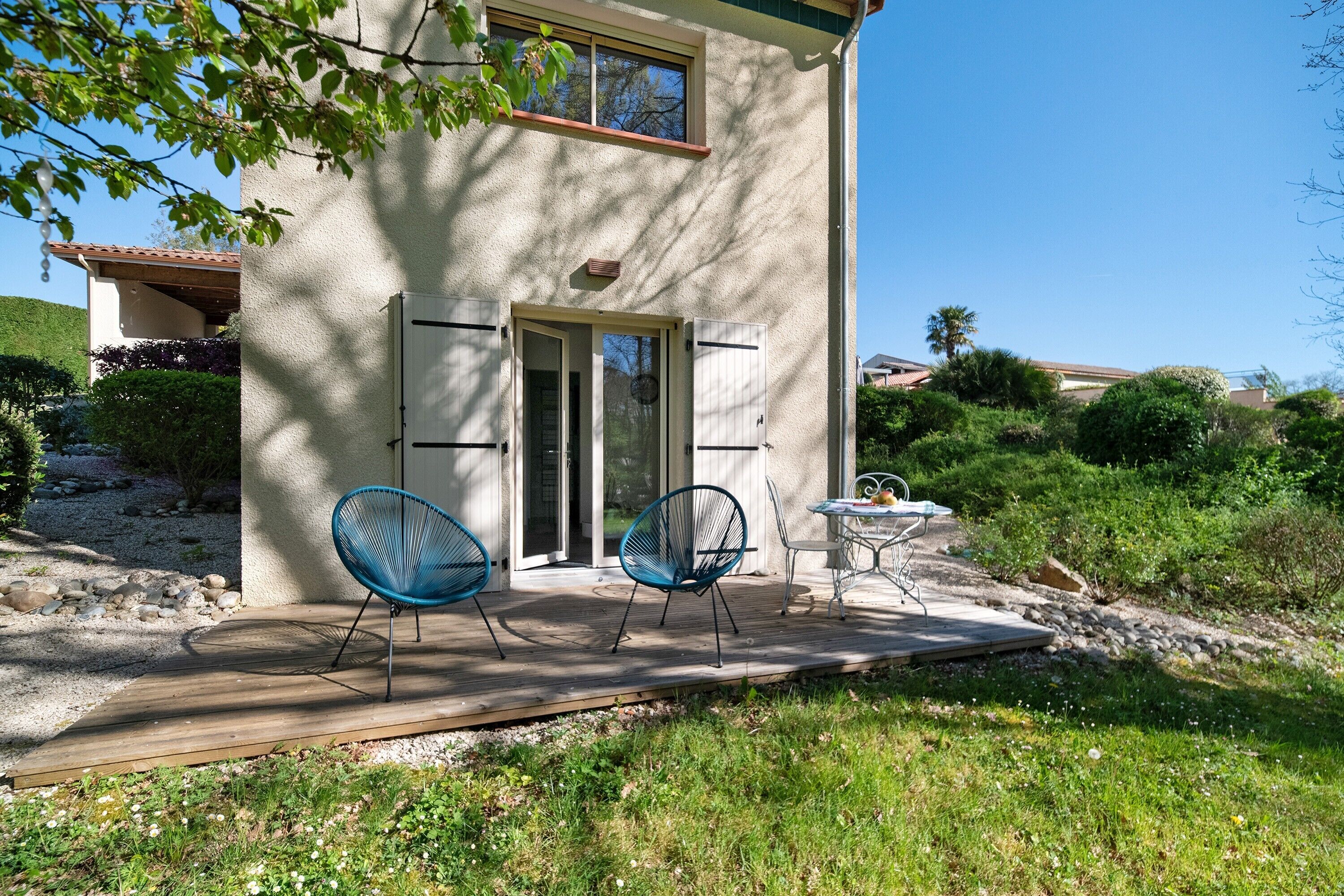 A house with a wooden deck, two blue chairs, and a small table.