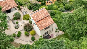 Ein Haus mit Ziegeldach, umgeben von einem Garten mit verschiedenen Sträuchern und einer gepflasterten Fläche.